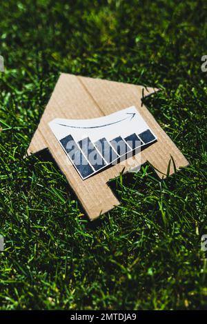 i tassi di interesse che scendono, grafico che mostra le statistiche che diminuiscono sopra l'icona della casa fatta di cartone sul prato verde Foto Stock