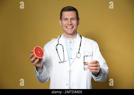 Nutrizionista che tiene un bicchiere di acqua pura e pompelmo maturo su fondo giallo Foto Stock