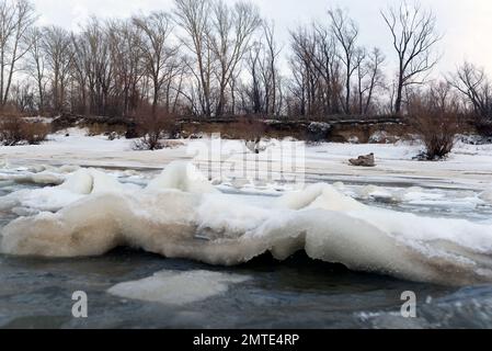 Il primo ghiaccio debole sorge in onde dal flusso d'acqua vicino alla riva. Foto Stock