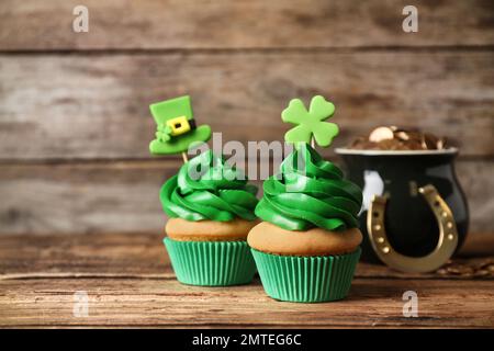 Cupcake decorati e pentola con monete d'oro su tavolo di legno. Festa di San Patrizio Foto Stock