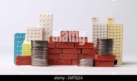 Un mucchio di monete con edifici in miniatura e mattoni rossi. Business concept con monete e miniatura. Foto Stock