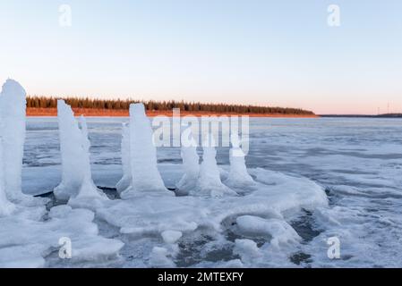 I resti di pilastri di ghiaccio ritagliati per l'acqua potabile si sciolgono in piedi sul ghiaccio del fiume in primavera al tramonto sullo sfondo Foto Stock