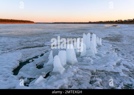 I resti di pilastri di ghiaccio ritagliati per l'acqua potabile si sciolgono in piedi sul ghiaccio del fiume in primavera al tramonto sullo sfondo Foto Stock