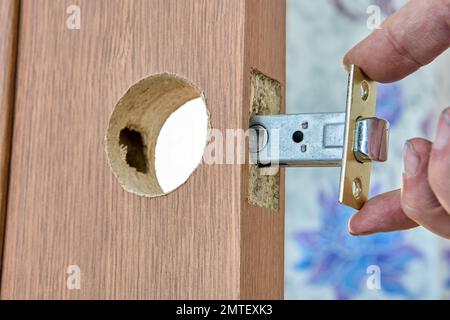 Il fabbro installa il pomello della porta con il fermo sulla porta interna in legno. Foto Stock