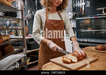 Lavoratore di panetteria positivo taglio pane fresco trecciato Foto Stock