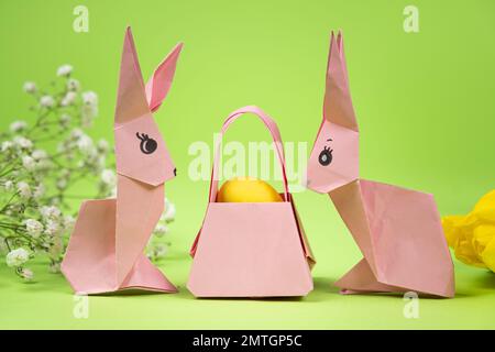 Origami di Pasqua - due coniglietti di carta e un uovo, sfondo verde. Artigianato per le vacanze, fatelo da soli. Foto Stock