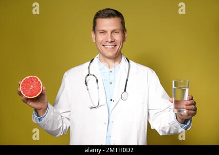 Nutrizionista che tiene un bicchiere di acqua pura e pompelmo maturo su fondo giallo Foto Stock