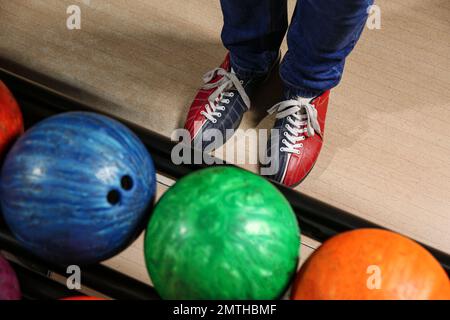 Persona in scarpe da bowling vicino al rack con palle, vista dall'alto Foto Stock