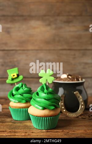 Cupcake decorati e pentola con monete d'oro su tavolo di legno. Festa di San Patrizio Foto Stock