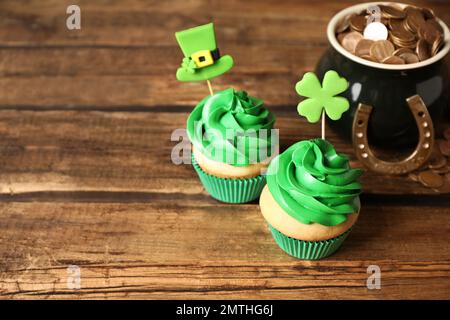Cupcake decorati e pentola con monete d'oro su tavolo di legno. Festa di San Patrizio Foto Stock