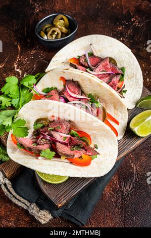 Carne Asada Tacos con bistecca alla griglia, salsa verde, jalapenos e cipolla, cibo messicano. Sfondo scuro. vista dall'alto. Foto Stock