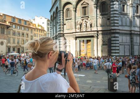 Foto femminile, vista posteriore di una giovane donna con una fotocamera che scatta una foto dell'edificio del Battistero di epoca rinascimentale a Firenze Foto Stock