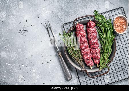 Kebab di Urfa Turco crudo decorato con erbe, spezie e forchetta di carne. Sfondo grigio. Vista dall'alto. Spazio di copia. Foto Stock