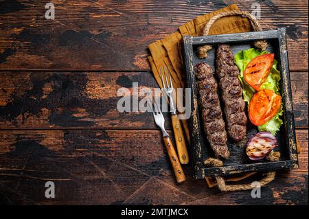 Tradizionale kefta mediorientale o kebab kofta, carne di manzo macinata e carne di agnello grigliata su spiedini serviti con pomodoro, insalata e cipolla. Sfondo di legno. In alto Foto Stock
