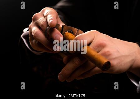 Foto ravvicinata di un maschio che tiene una ghigliottina e un sigaro. Le mani degli uomini tagliano un sigaro con le forbici. Foto Stock