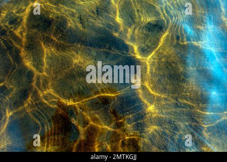 Foto astratta della texture del riflesso di luce dalla superficie delle onde di acqua chiara trasparente in movimento nei toni gialli luminosi. Foto Stock