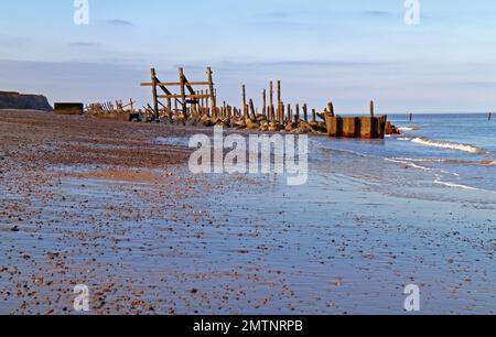 Una vista delle vecchie difese abbandonate del mare in acqua bassa in un tranquillo pomeriggio d'inverno sulla costa di Norfolk a Happisburgh, Norfolk, Inghilterra, Regno Unito. Foto Stock