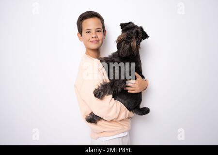 Il cane Schnauzer e il ragazzo sorridente la abbraccia con tenerezza e guardano la telecamera su sfondo giallo. Animali domestici. Emozioni della gente. Infanzia. Stile di vita. PET c Foto Stock