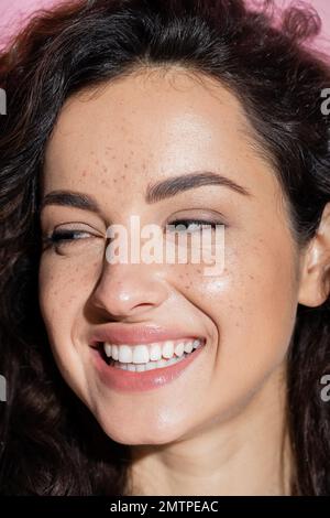 Ritratto di donna sorridente con lentiggini guardando lontano isolato su rosa, immagine stock Foto Stock