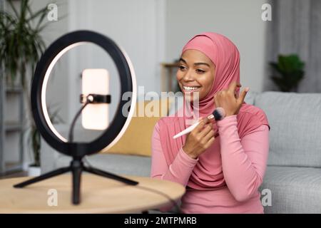 Blog di bellezza. Donna afroamericana in hijab making make and recording video tutorial per il suo blog Foto Stock