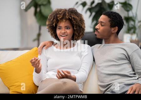 Uomo e donna afro-americana seduti sul divano, parlando Foto Stock