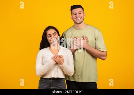 Allegro rilassato giovane donna e ragazzo arabo in casual con gli occhi chiusi mettere le mani al petto Foto Stock