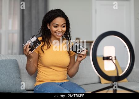 Felice afroamericana donna riprese video per il suo blog, facendo recensione su fotocamere retro, parlando su smartphone Foto Stock