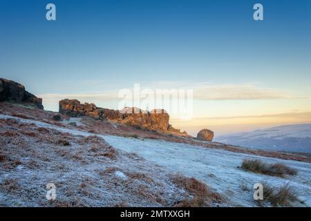 Un paesaggio stupefacente dell'alba alle rocce di vitello e di mucca sopra Ilkley con il sole che colpisce appena la faccia della roccia in una giornata molto fredda con il gelo che copre il Foto Stock