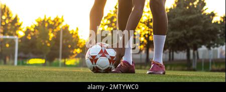 Il corpo inferiore di un giocatore di calcio ispanico che mette la palla sull'erba, retroilluminata dalla luce del sole Foto Stock