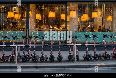 Voi scooter elettrici a noleggio allineati di fronte a una vetrina ristorante a Liverpool Foto Stock