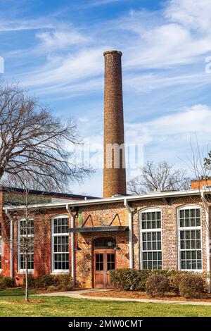 WAXHAW, NC, USA-28 GEN 2023: Fumetto di mattoni dietro un piano riproposto mulino edificio. Cielo azzurro e soleggiato. Foto Stock