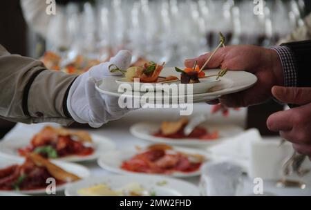 Il cameriere mette gli antipasti sul piatto dell'uomo durante il tavolo del buffet Foto Stock