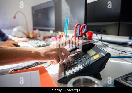 Mano di un dipendente che al lavoro risponde al telefono in ufficio Foto Stock