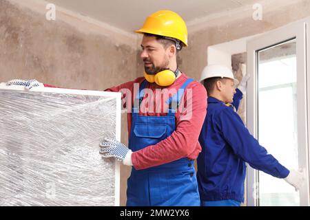 Lavoratori in uniforme installare finestre in plastica al chiuso Foto Stock