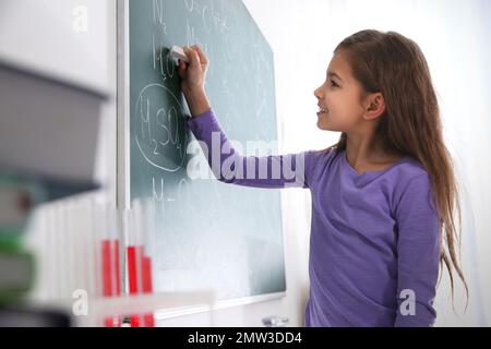 Schoolgirl scrivere formule chimiche sulla lavagna in classe Foto Stock