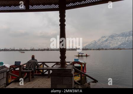 Srinagar, India. 01st Feb, 2023. Un uomo si siede su un Jetty davanti ad un barcaiolo che canora la sua barca durante una giornata nuvolosa a Srinagar. Credit: SOPA Images Limited/Alamy Live News Foto Stock