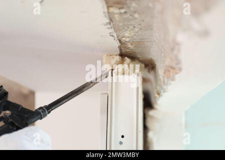 Lavoratore che utilizza la pistola per schiuma per l'installazione di finestre in ambienti chiusi, primo piano Foto Stock