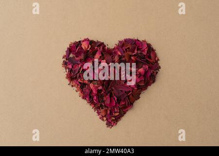 Cuore rosso in petali di rosa secchi. Fiori forma cuore rosso secco rose. Sfondo d'amore, carta giorno di San Valentino Foto Stock