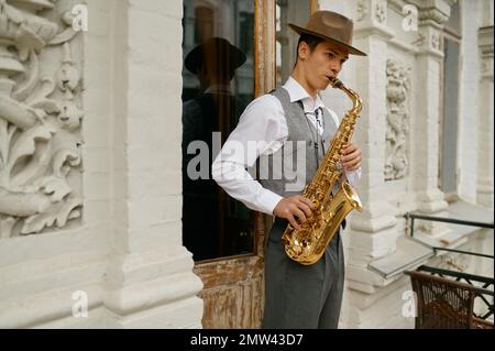 Giovane musicista maschile che pratica sassofono in balcone a casa Foto Stock