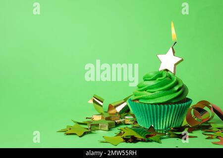 Delizioso cupcake di compleanno con candela accesa su sfondo verde. Spazio per il testo Foto Stock