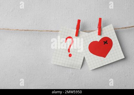 Note cartacee con disegni di cuore e punto interrogativo inchiodati sul filo del bucato vicino alla parete leggera. Concetto di problemi di relazione Foto Stock