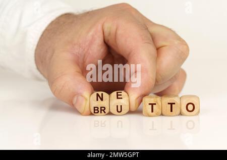 Su una superficie bianca riflettente nelle mani di un uomo sono cubi con l'iscrizione - NETTO o BRUTTO. Concetto aziendale. Foto Stock