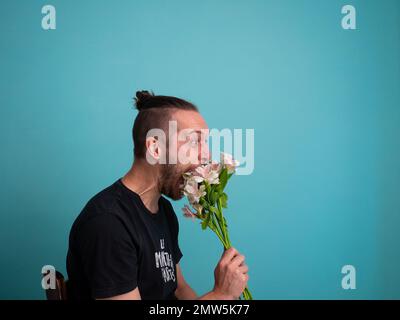 Arrabbiato uomo bianco che tiene fiori su uno sfondo turchese Foto Stock