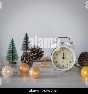 Una sveglia bianca, un puntatore a dodici, un piccolo albero di Natale verde artificiale e una ghirlanda su una cassettiera bianca. Spazio di copia. Biglietto di Natale. Foto Stock