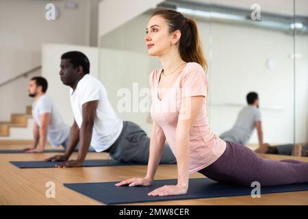 Donna che pratica il cobra posa con il gruppo in palestra Foto Stock