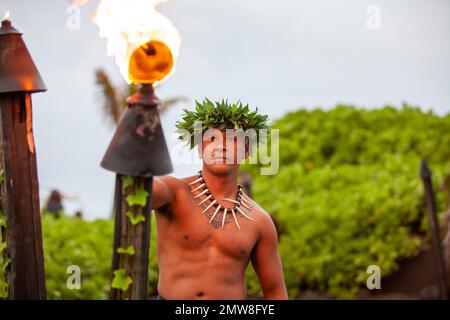 Uomo hawaiano in abito tradizionale che illumina una torcia prima dello spettacolo Foto Stock