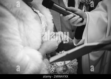 Un primo piano di una sposa e sposo che si scambiano gli anelli al loro matrimonio in scala di grigi Foto Stock