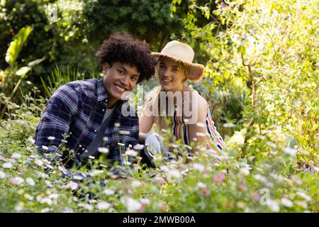 Ritratto di felice coppia diversi giardinaggio, seduto tra i fiori in giardino soleggiato Foto Stock