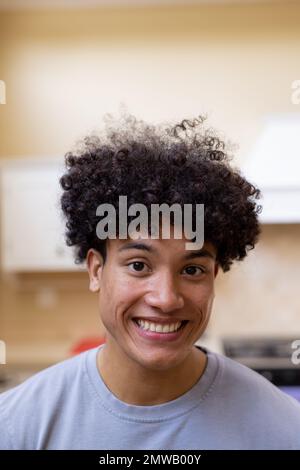 Ritratto verticale di un uomo biraciale sorridente con capelli ricci in cucina a casa Foto Stock