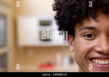 Ritratto a metà faccia di un uomo biraciale sorridente con capelli ricci in cucina a casa, copia spazio Foto Stock